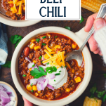 Overhead shot of hands eating a bowl of beef chili with a spoon and text title overlay.