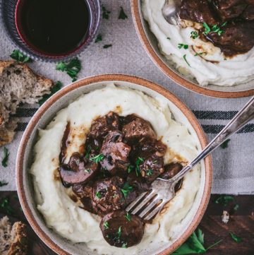 Two bowls of mashed potatoes with crockpot beef tips and gravy on a dinner table.
