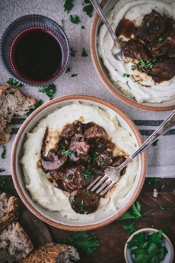 Two bowls of mashed potatoes with crockpot beef tips and gravy on a dinner table.