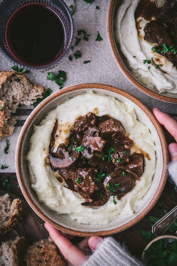 Overhead shot of hands holding a bowl of beef tips and gravy over mashed potatoes.