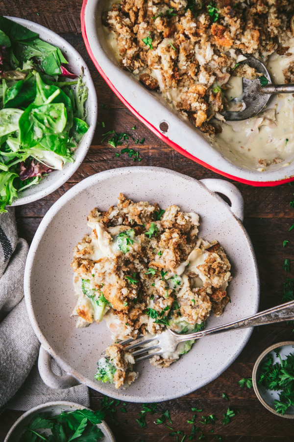 Overhead image of a bowl of chicken broccoli stuffing casserole on a dinner table with a side salad.