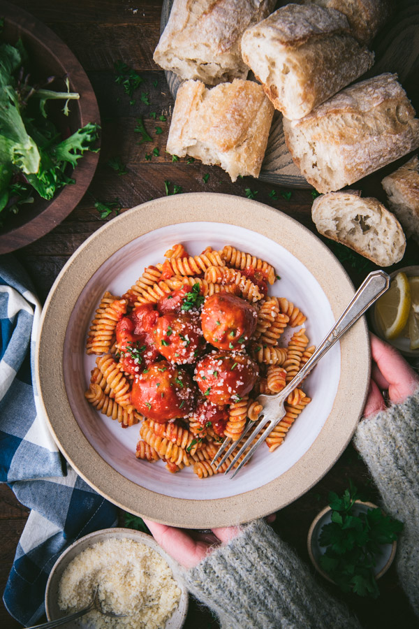 Overhead shot of hands holding a bowl of pasta with baked chicken meatballs