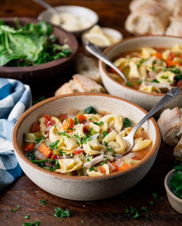 Side shot of chicken tortellini soup recipe in two bowls on a table with a salad and bread.