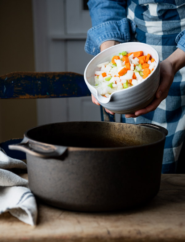 Adding diced vegetables to a Dutch oven.