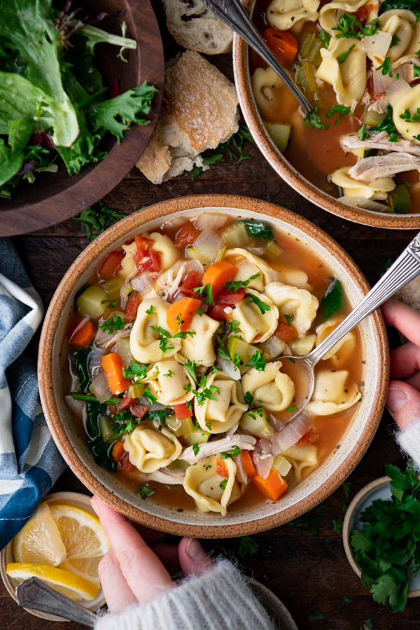 Overhead shot of hands holding a bowl of chicken tortellini soup.