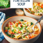 Side shot of chicken tortellini soup with spinach and text title overlay