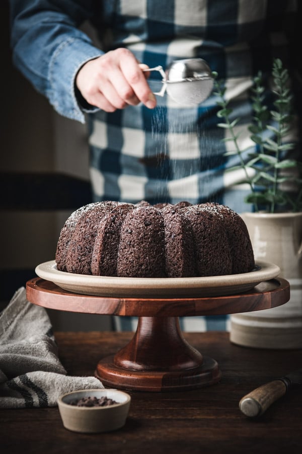 Dusting chocolate pudding bundt cake with powdered sugar.