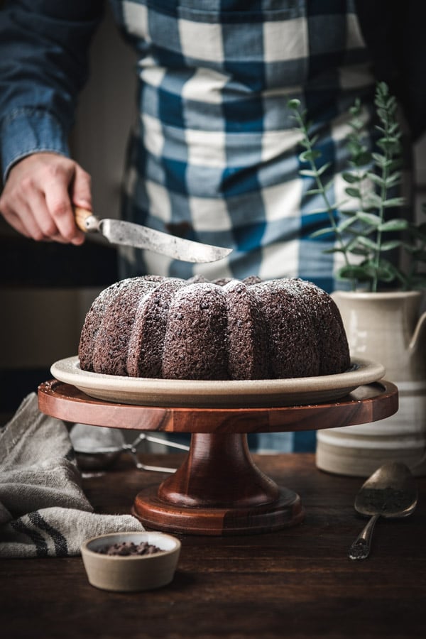 Slicing a chocolate sour cream bundt cake with a large knife.