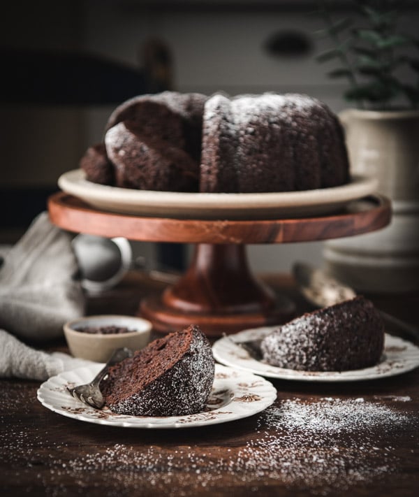 Two slices of chocolate bundt cake on plates with the cake in the background.