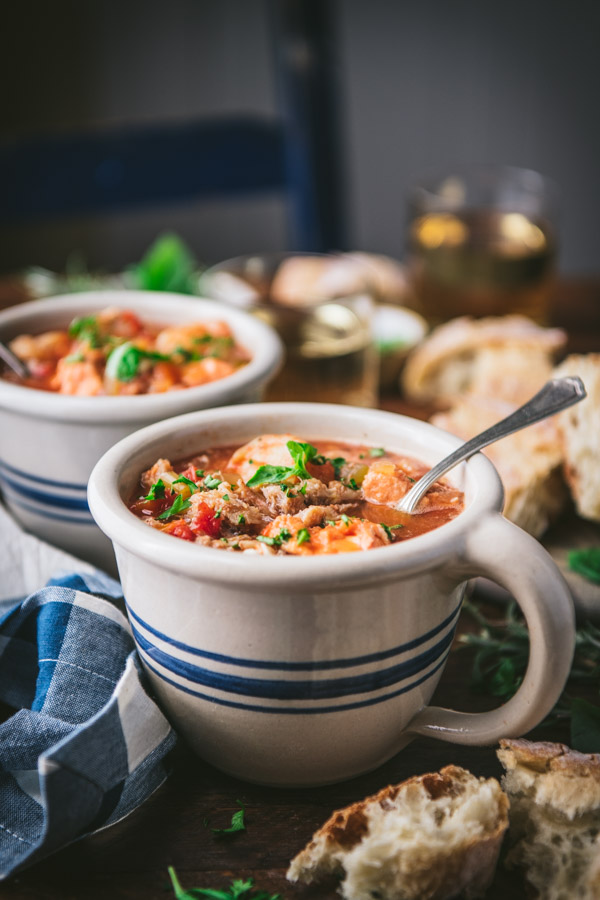 Close up side shot of cioppino soup with bread and wine in the background