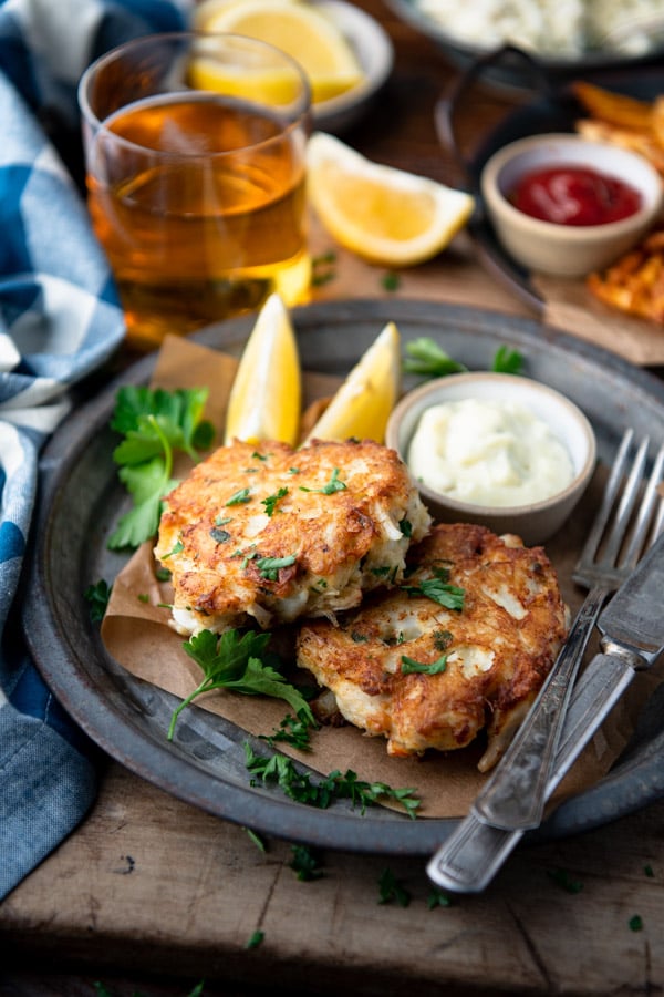Side shot of crab cakes on a plate with beer and french fries in the background