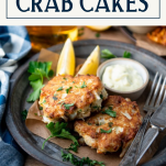Side shot of a plate of two crab cakes with text title box at top