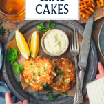 Hands holding a plate of crab cakes with text title overlay