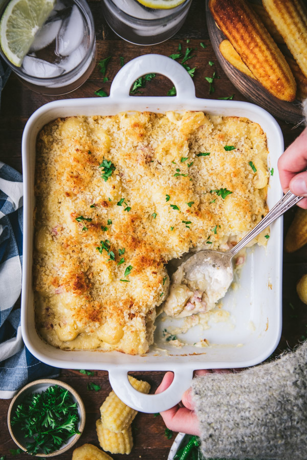 Hands serving ham and cheese casserole from a white baking dish.