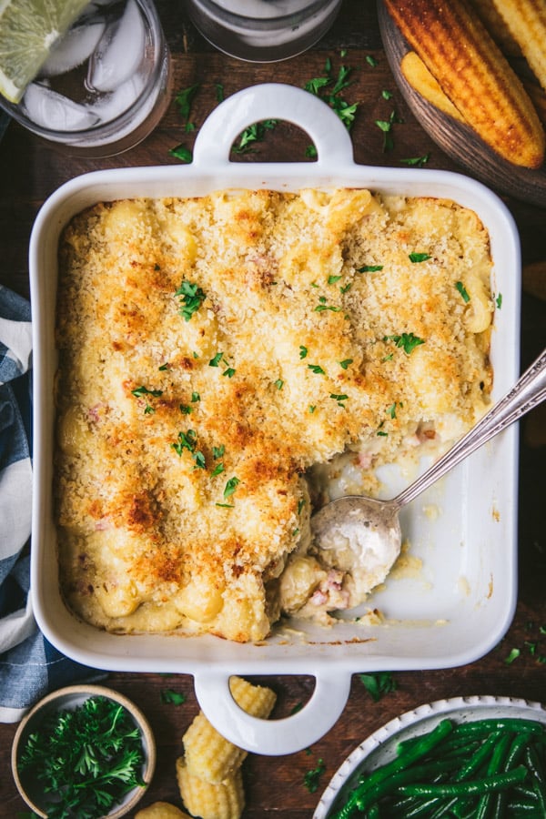 Overhead shot of baked mac and cheese with ham in a white dish with a serving spoon.