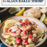 Side shot of a bowl of the best baked shrimp recipe served over pasta with text title box at top
