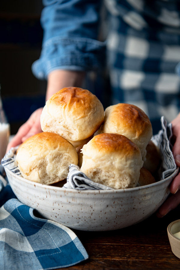Hands serving a bowl of easy dinner rolls on a wooden table