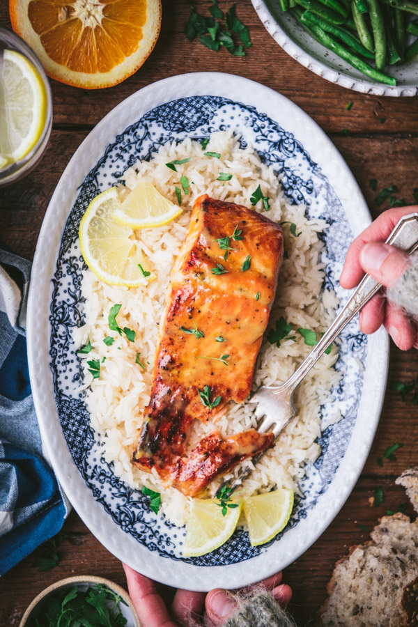 Overhead image of hands eating a piece of orange salmon with a fork.