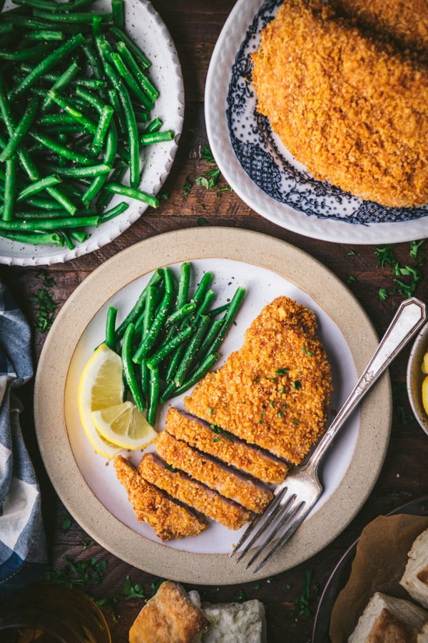 Oven fried pork chops on a plate with lemon wedges and green beans.