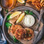 Overhead shot of three salmon patties on a plate with a side of fries and coleslaw