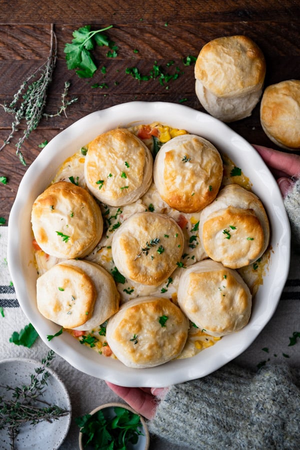 Overhead shot of hands holding a pan of chicken pot pie with biscuits