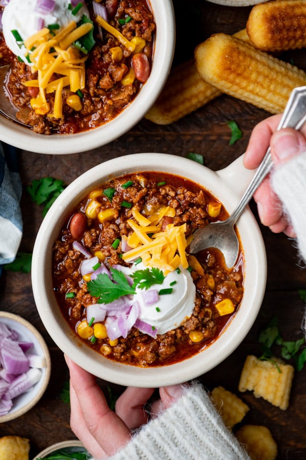Overhead shot of hands eating a bowl of easy chili recipe with a spoon.
