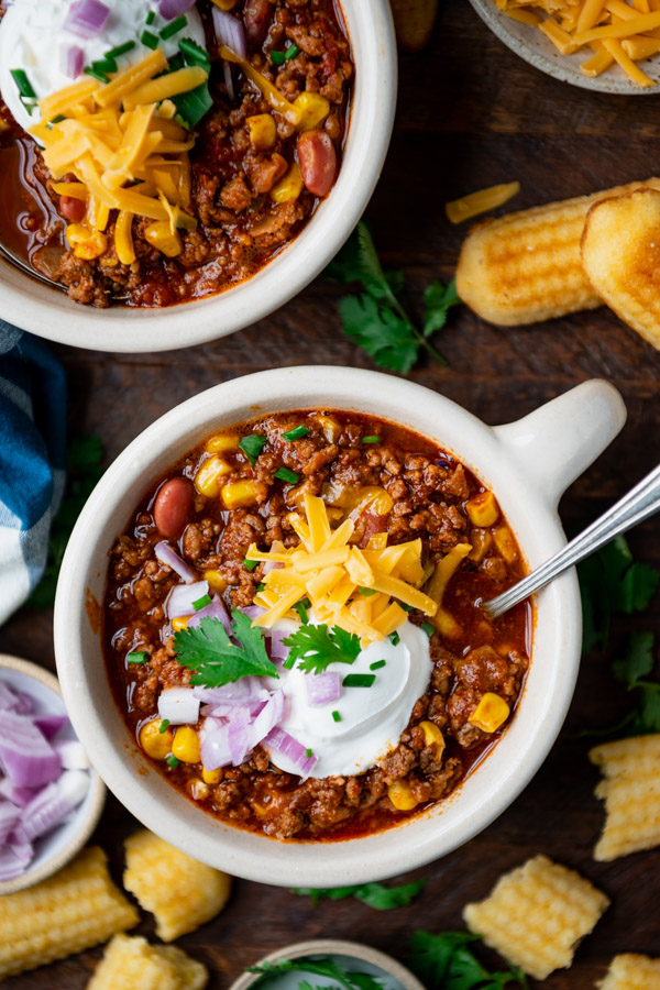 Close overhead image of classic beef chili in bowls with toppings.