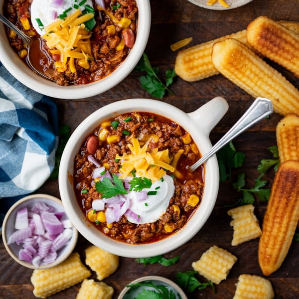 Bowls of the best slow cooker chili recipe on a table with a side of cornbread.