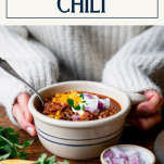 Hands holding a bowl of crockpot chili with text title box at top.