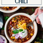 Close overhead shot of a spoon in a bowl of slow cooker chili with text title box at top.