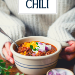 Hands holding a bowl of the best slow cooker chili recipe with text title overlay