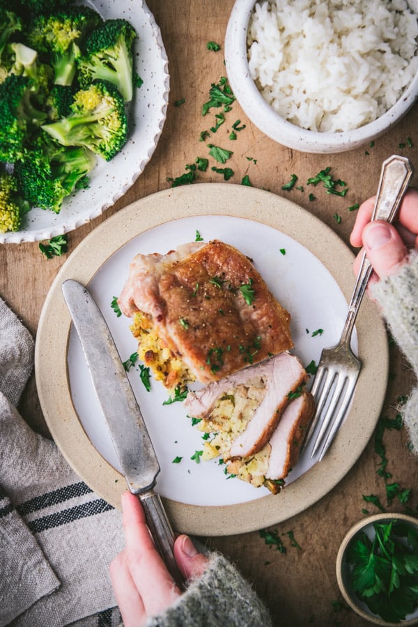 Overhead shot of hands eating baked stuffed pork chops on a plate with a side of broccoli