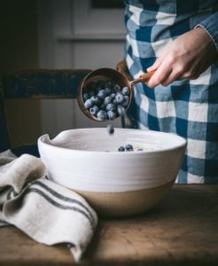 Adding blueberries to a white bowl.
