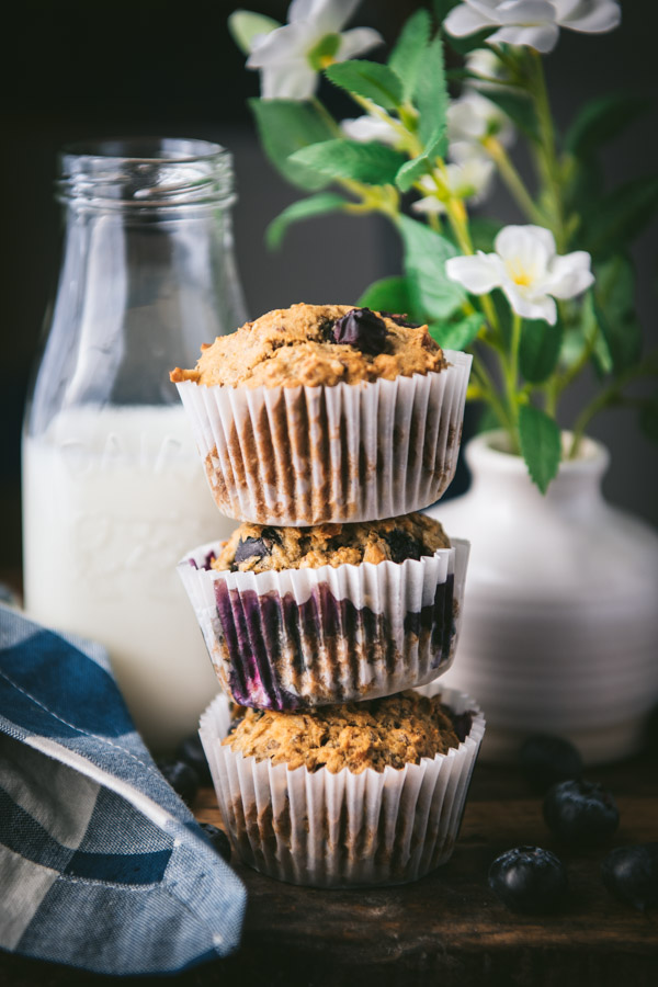 Three banana blueberry muffins with oatmeal stacked on a wooden table.