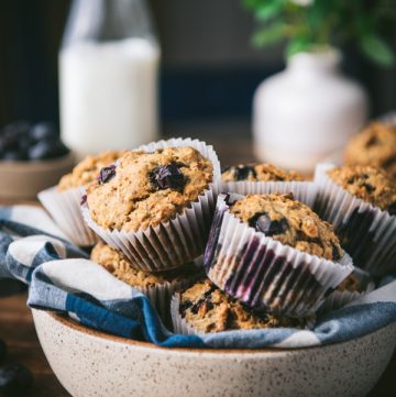 Bowl of whole wheat banana blueberry muffins with milk in the background.
