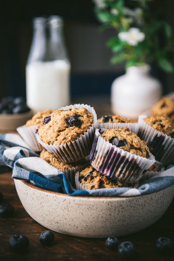 Bowl of whole wheat banana blueberry muffins with milk in the background.