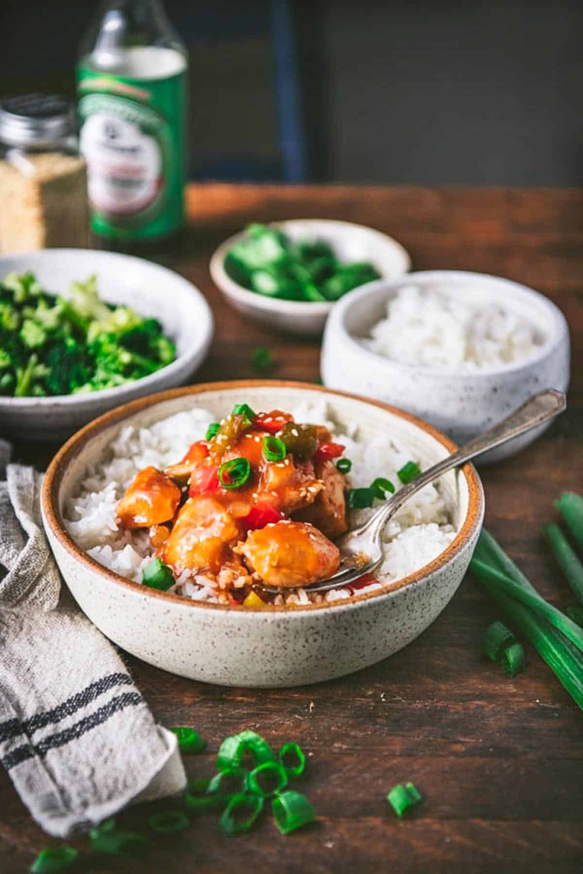 Side shot of Chinese baked sweet and sour chicken on a table with rice and broccoli.