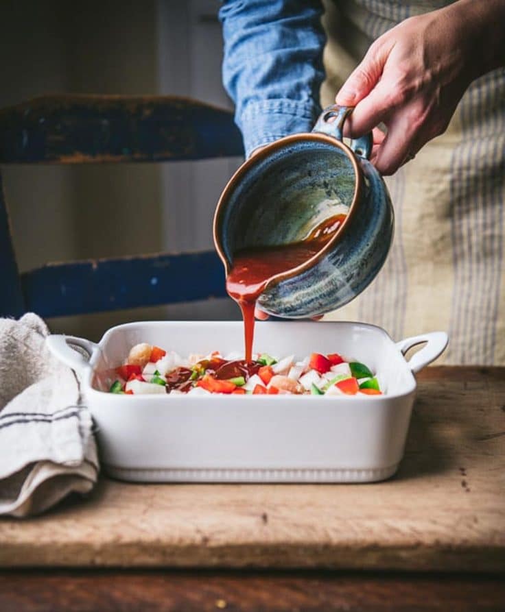 Pouring homemade sweet and sour sauce for chicken over a dish of meat and veggies.