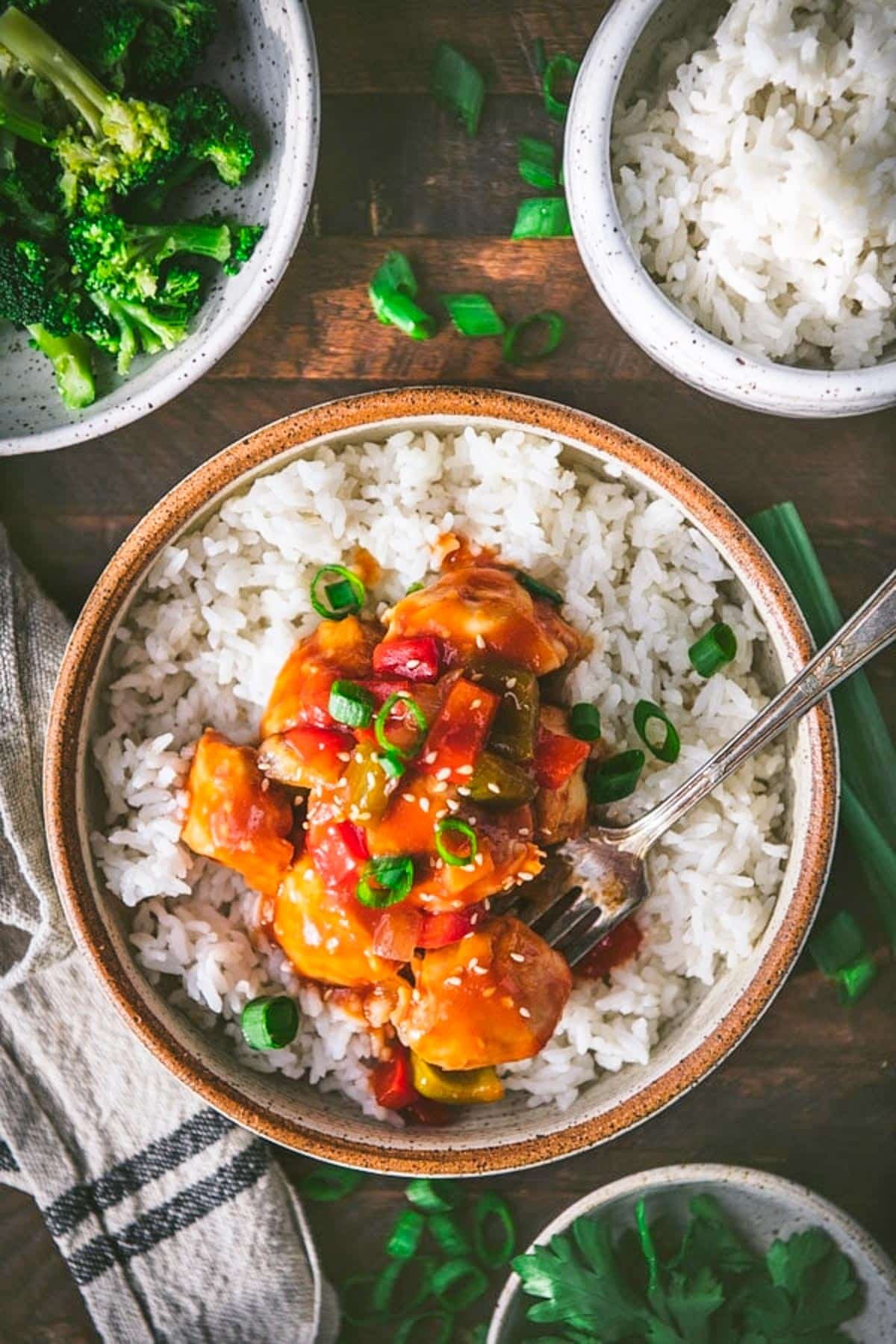 Overhead image of a bowl of sweet and sour baked chicken on top of rice and garnished with green onions.