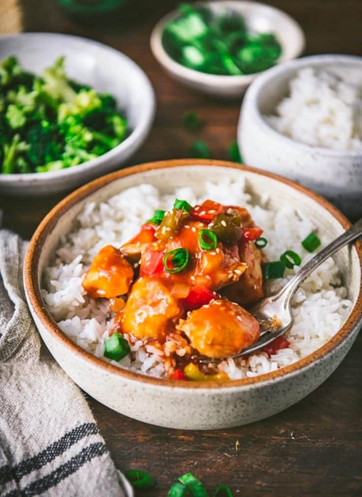 Close up side shot of baked chicken sweet and sour with rice on a table with broccoli in the background.