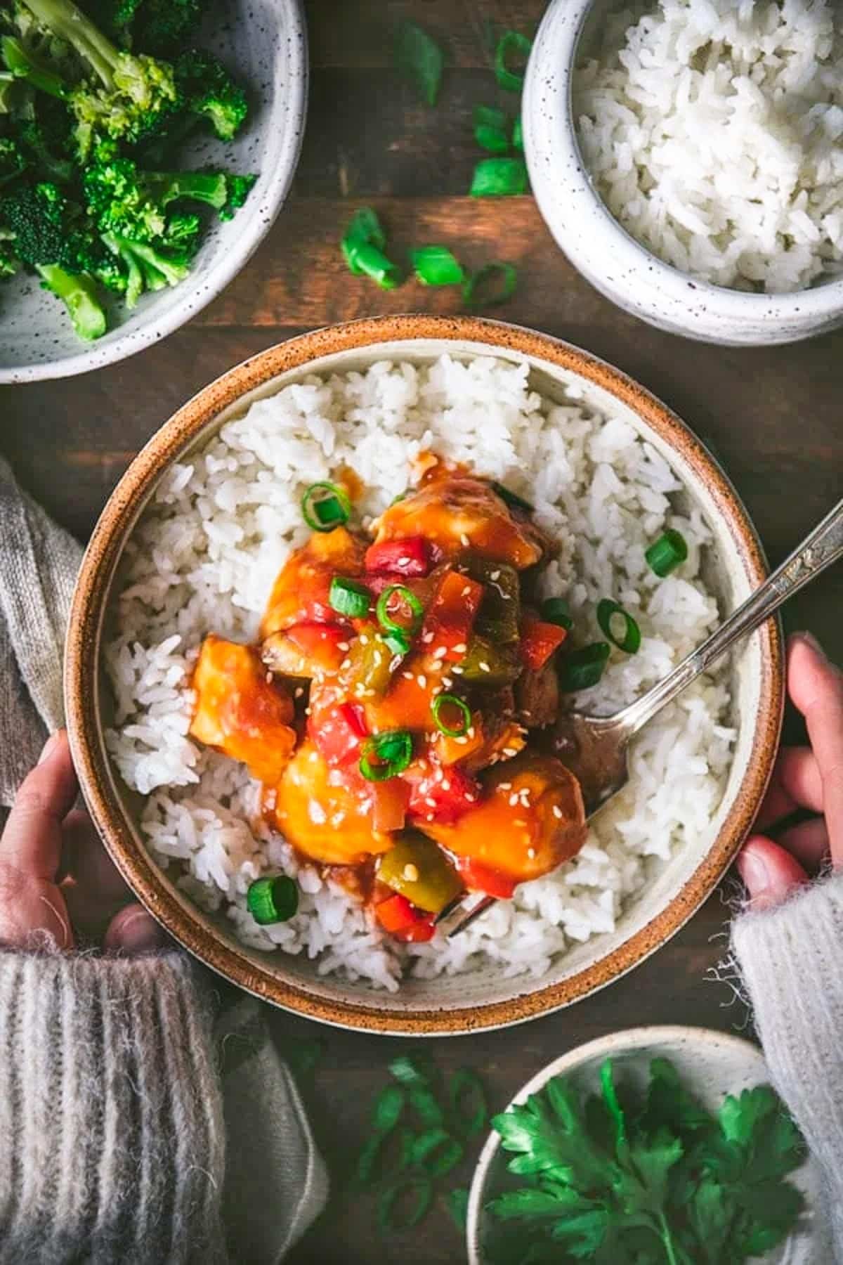 Overhead shot of hands holding a bowl of easy baked sweet and sour chicken without frying.
