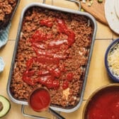 Process shot showing how to layer the ingredients for a beef enchilada casserole.
