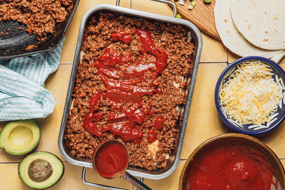 Process shot showing how to layer the ingredients for a beef enchilada casserole.