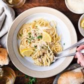 Square overhead shot of a bowl of linguine with clam sauce garnished with lemons and parsley.