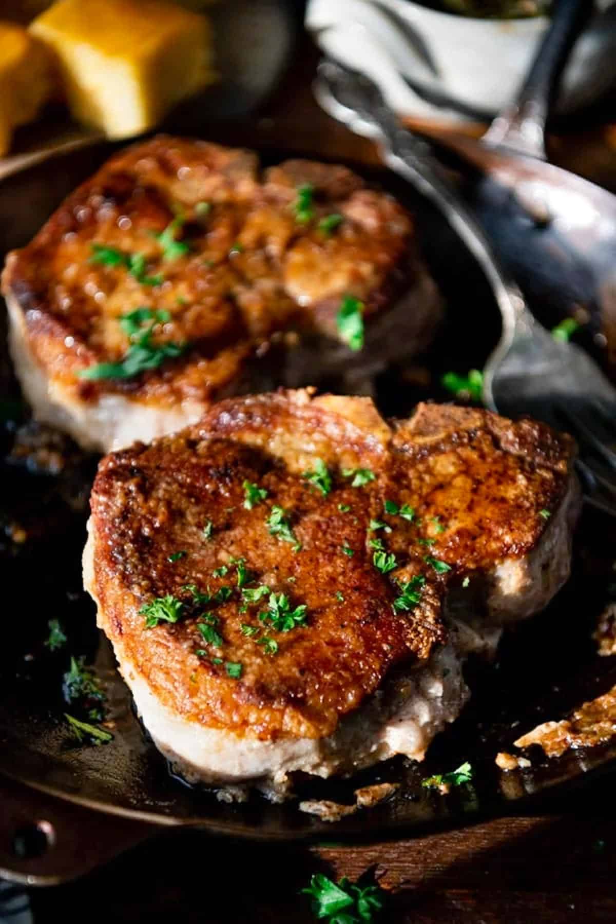 Close up side shot of thick pan fried pork chops in a skillet.