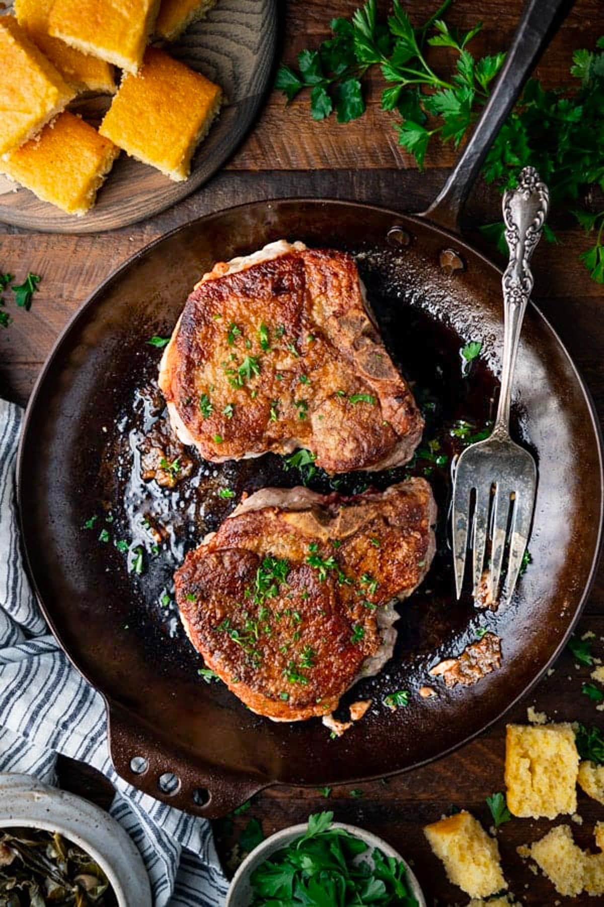 Overhead image of pan fried pork chops in a skillet with fresh parsley garnish.