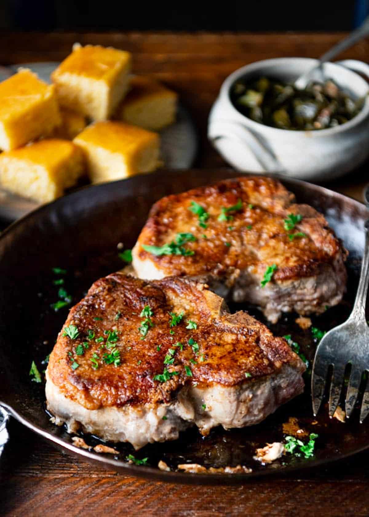Side shot of thick cut pork chops pan fried in a skillet.