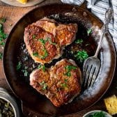 Square overhead shot of two pan fried pork chops in a cast iron skillet.
