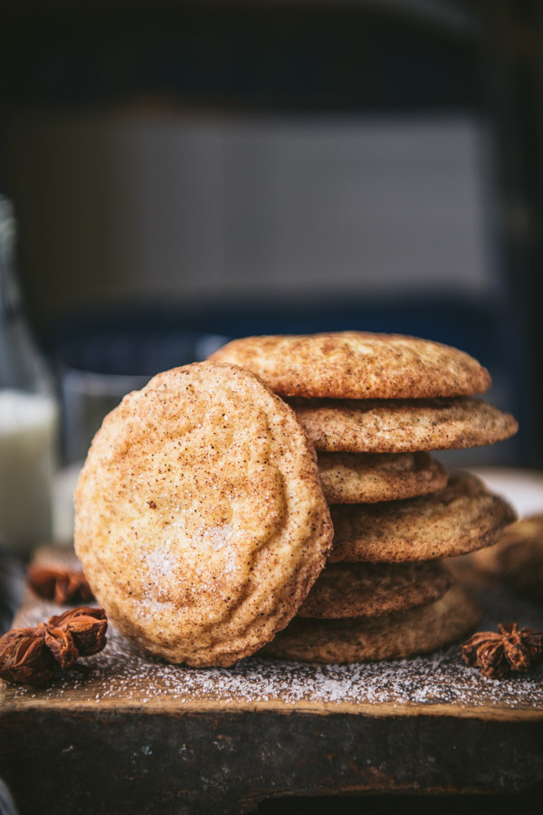 Side shot of a stack of snickerdoodle cookies on a wooden board with milk in the background