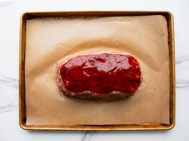 Spreading the ketchup glaze on top of a Southern meatloaf before baking.